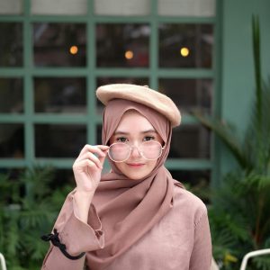 Charming woman wearing hijab and beret, posing elegantly in a modern setting.